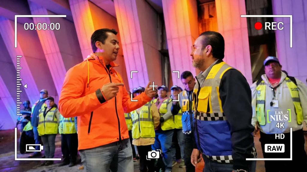 Dos hombres conversando frente a trabajadores viales con chalecos reflejantes en obras de Bernardo Quintana, de noche